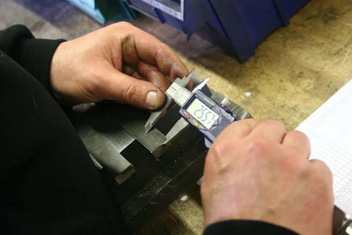 Hands using a digital caliper to measure a metal part