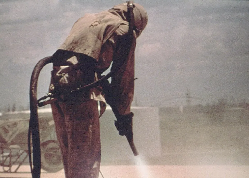 Worker in full protective gear abrasive-blasting a surface